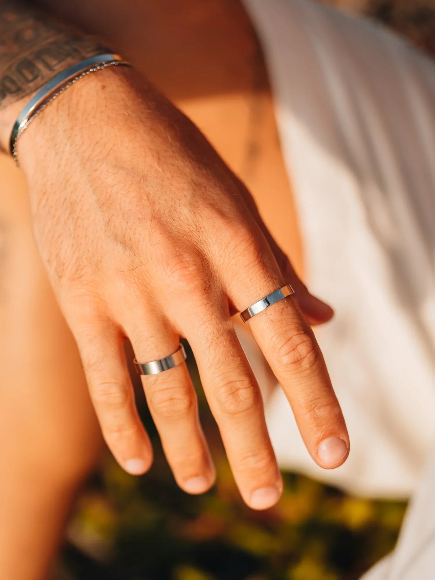 יד של גבר עם שתי טבעות כסף מינימליסטיות על האצבעות ברקע חוף וטבע