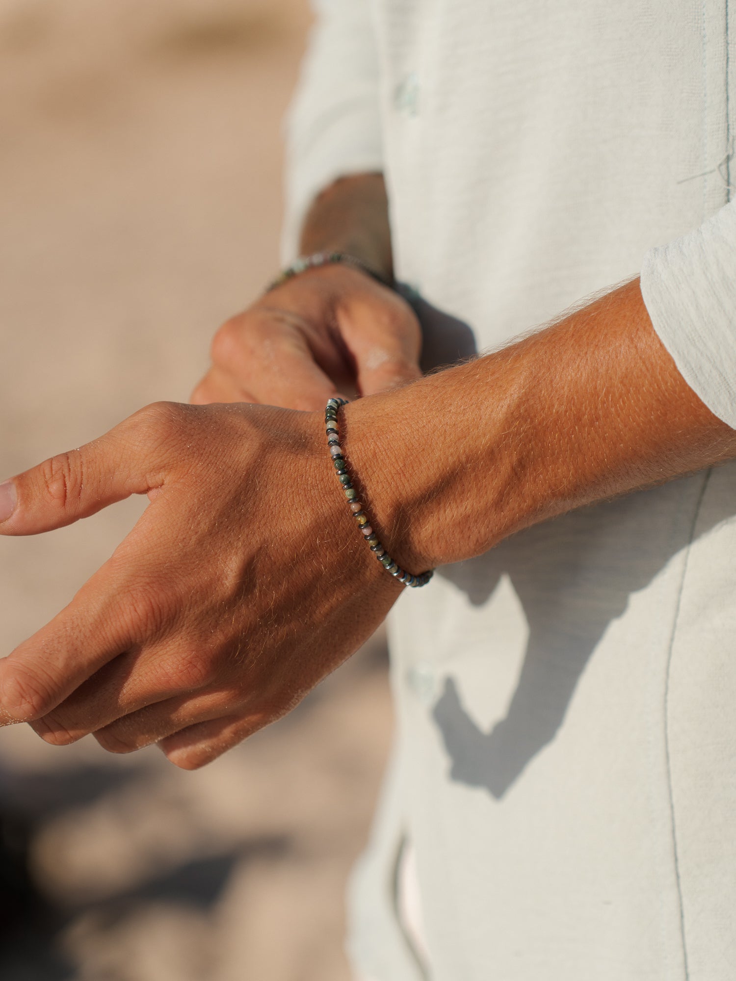 צמיד Tulum לגבר (המטיט ואגט) על פרק יד בחוף, צילום תקריב המדגיש את טקסטורת האבן.