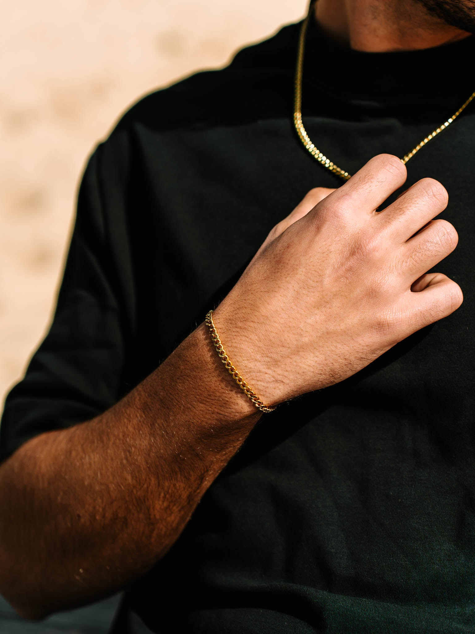 צמיד Zeus מוזהב על פרק יד של גבר שלובש חולצה שחורה ושרשרת זהב תואמת